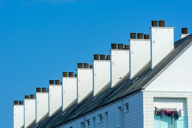 Row of chimneys on modern residential buildings under a clear blue sky. Urban architecture with rooftops. Profitable chimney sweep services: the parts worth your attention